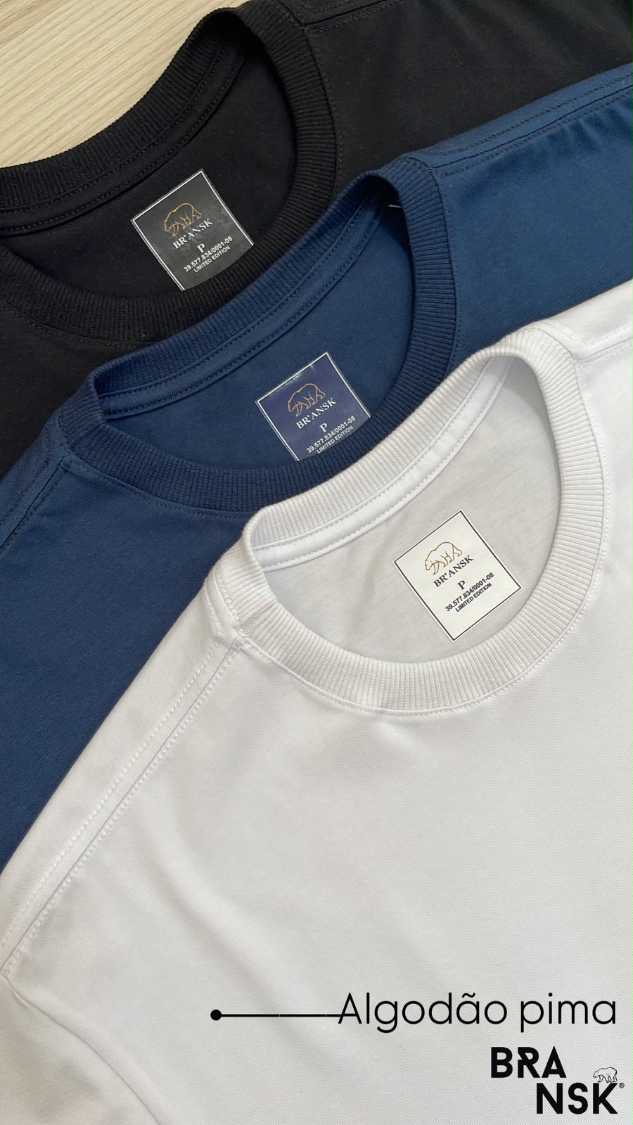 Três camisetas Bransk de algodão pima dobradas, nas cores preta, azul-marinho e branca, com etiqueta interna da marca